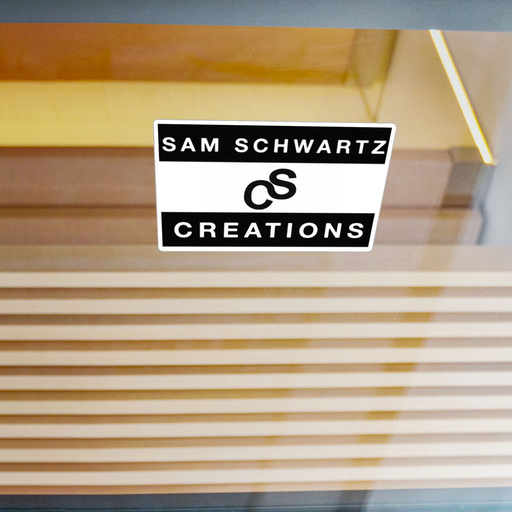 A rectangular black and white sticker with the text 'SAM SCHWARTZ CREATIONS' and a stylized ampersand logo, shown on a glass door with a blurred background of vertical wooden slats.